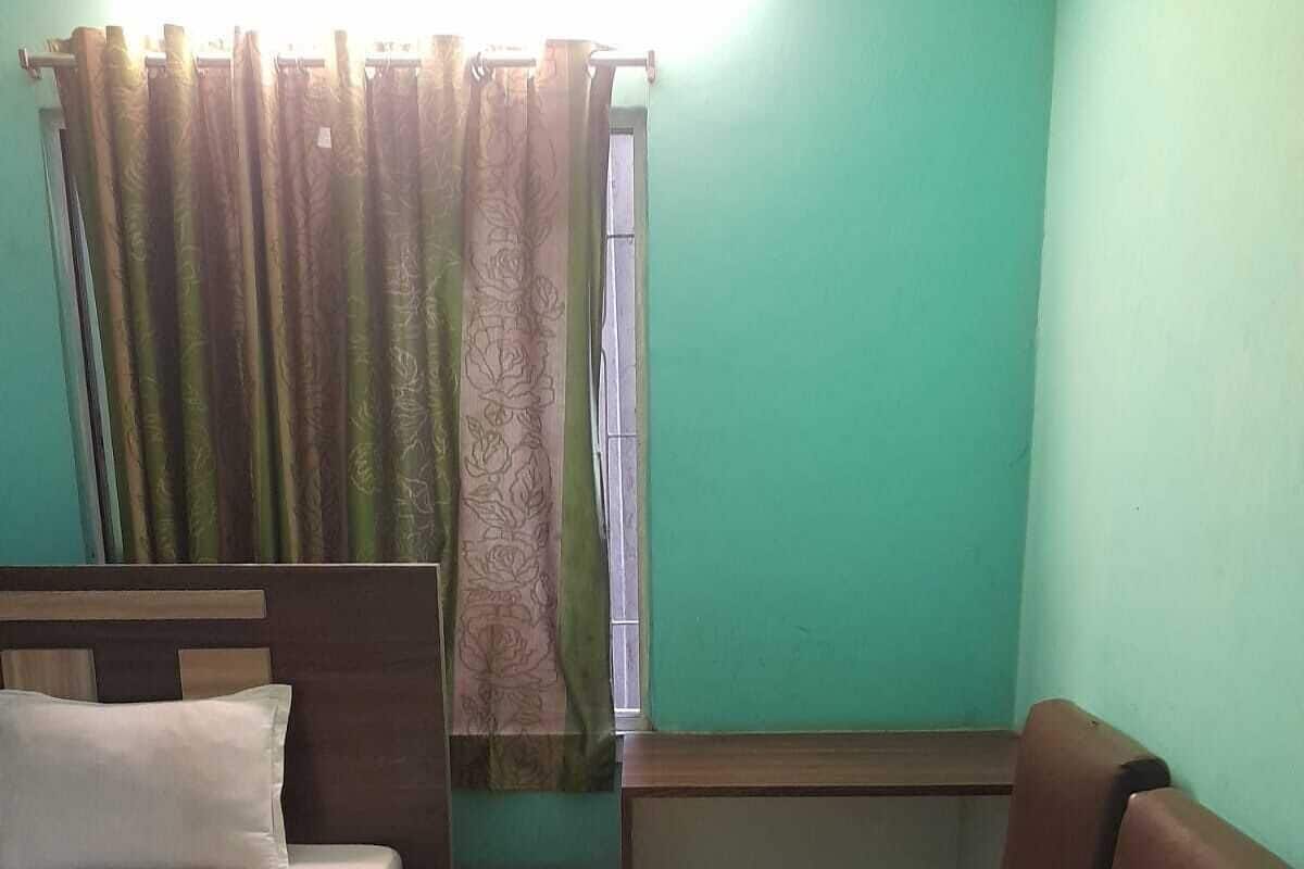 Um quarto pequeno com cama, escrivaninha, cadeira e janela com cortinas.