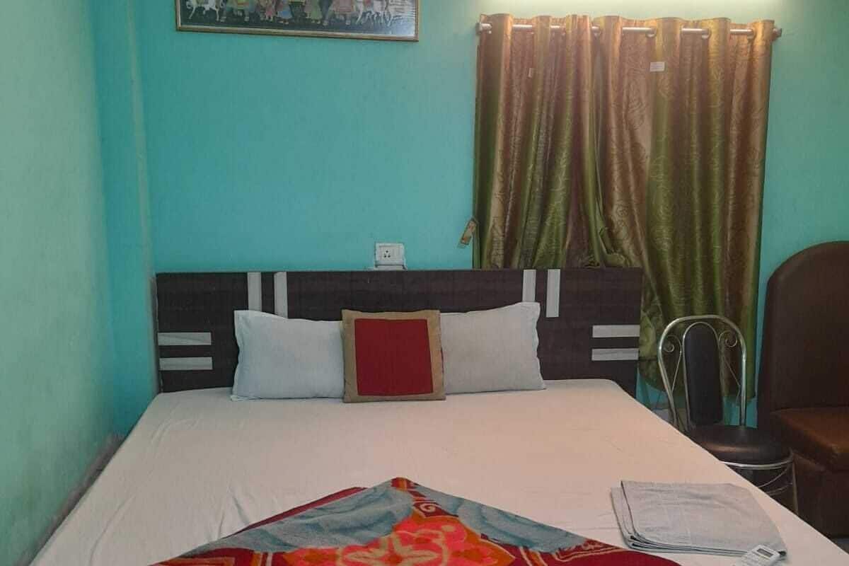 Uma cama de solteiro com cabeceira, mesa de cabeceira, cadeira, cortina e luminária fixada na parede.