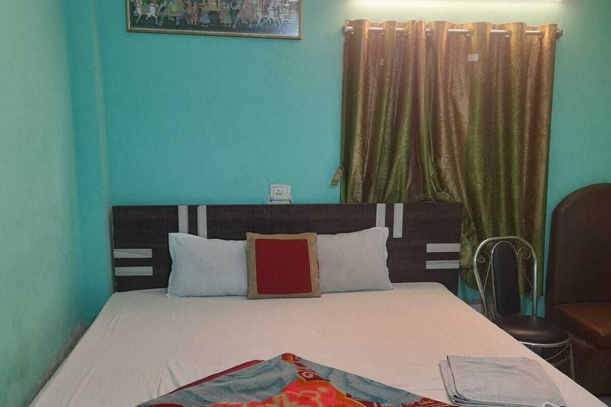 Uma cama com um edredom estampado, cabeceira e luminária fixada na parede.