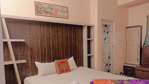 Quarto com cama, cabeceira de madeira, porta com detalhes decorativos e uma pequena mesa com cadeira.