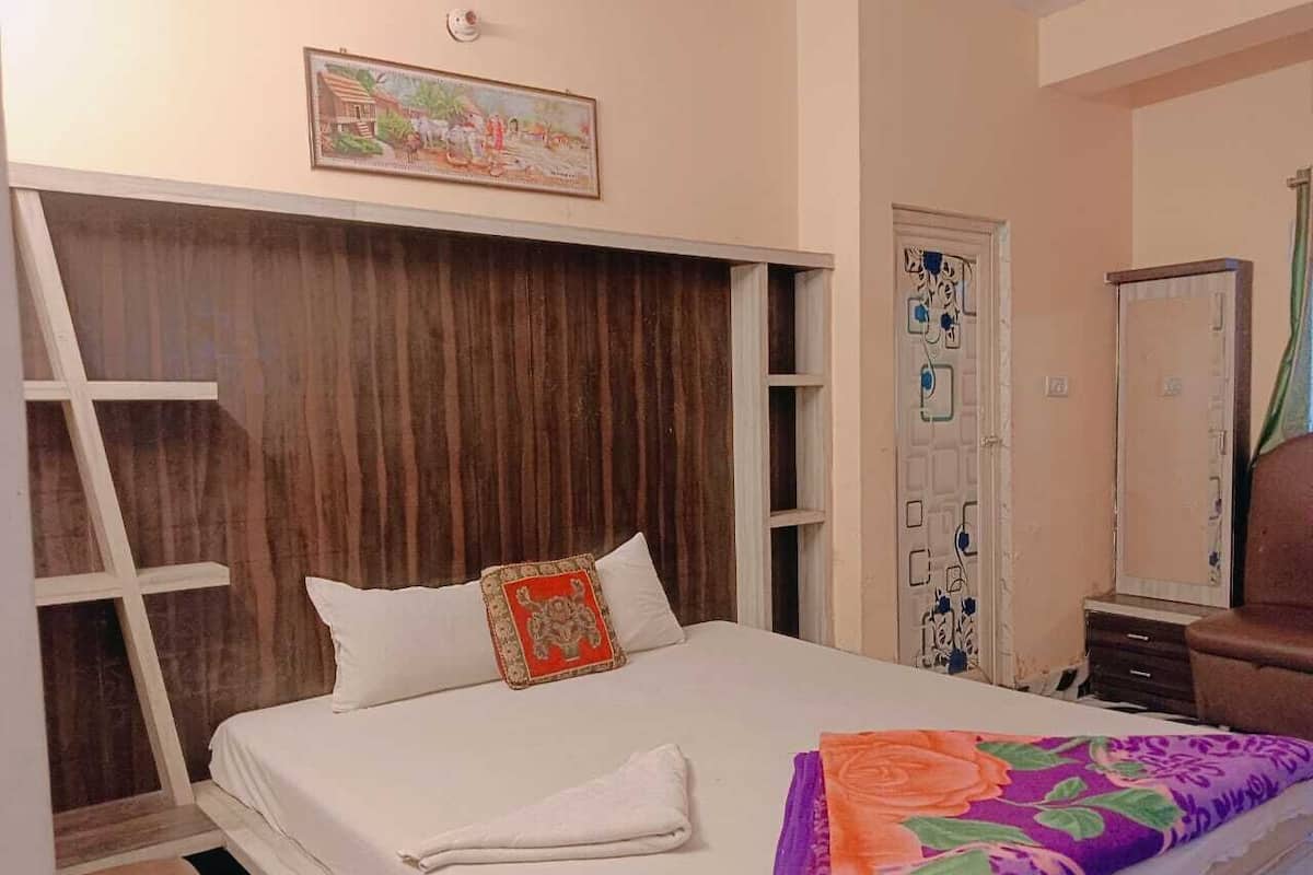 Quarto com cama, cabeceira de madeira, porta com detalhes decorativos e uma pequena mesa com cadeira.