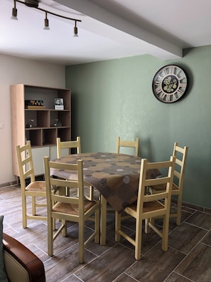 Un comedor con una mesa redonda, cuatro sillas, una estantería de madera y un reloj montado en la pared.