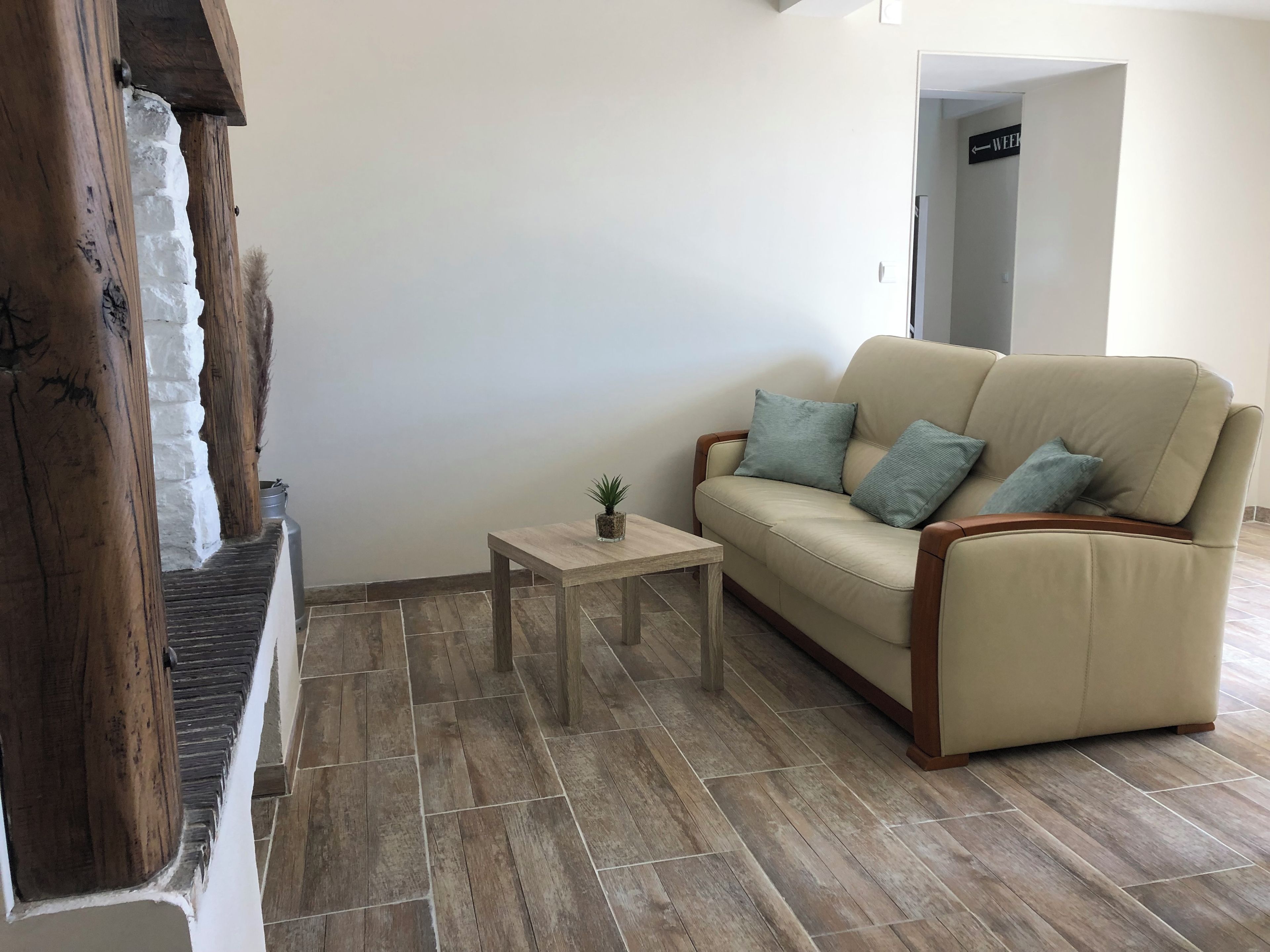 Een woonkamer met een beige bank, een klein houten bijzettafeltje en een potplant.