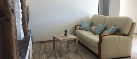 En stue med en beige sofa, et lille træbord og en potteplante.