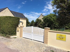 A gated entrance to a property with a stone facade, a white gate, and a yellow sign with text.