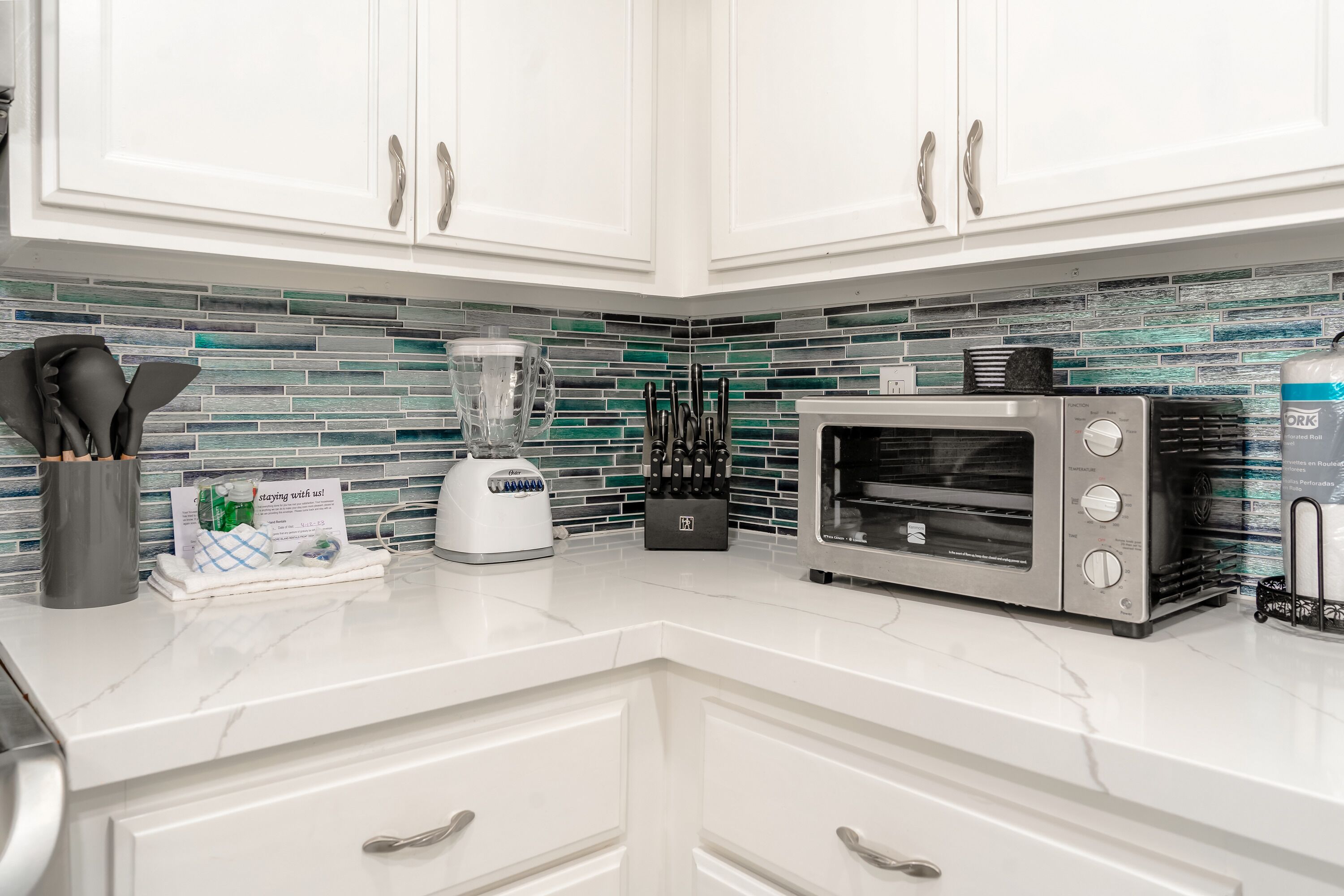 A kitchen with white cabinets, a toaster, a blender, and a toaster oven.