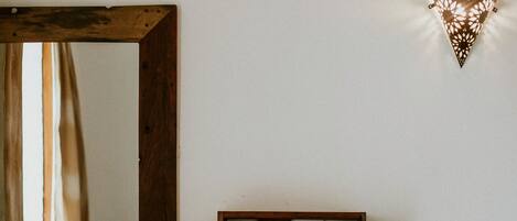 Une pièce avec un grand miroir, une étagère en bois et un luminaire fixé au mur.