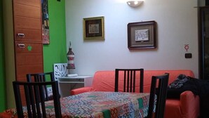 A dining area with a table set for four, surrounded by chairs, a red sofa, and a cabinet against a green wall.