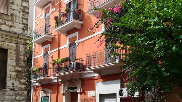 A multi-story building with balconies, a closed shuttered door, and a sign with text.