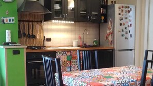 A kitchen with a dining table, chairs, a clock, cabinets, a stove, and a refrigerator.