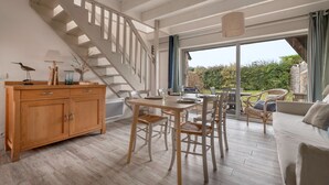 A spacious living area with a wooden dining table, wicker chairs, a sofa, and a staircase leading to a balcony. - House for 5 at a few steps from the beach (Arzon)