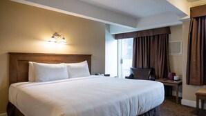 A large bed with a wooden headboard, a bedside table, and a chair. - Standard King Room in Banff with Air-Conditioning (Banff)