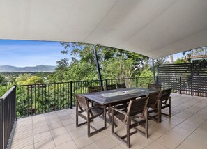 Enjoy dining or socializing in this outdoor patio area with a table and chairs, surrounded by lush greenery and distant mountains.