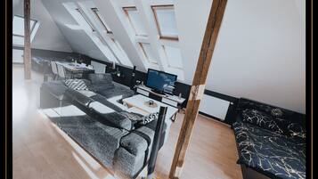 A modern loft bedroom with skylights, a sofa, a TV, and a dining area.