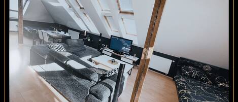 Une chambre de style loft moderne, dotée de fenêtres de toit, d’un canapé, d’une télévision et d’un coin repas.