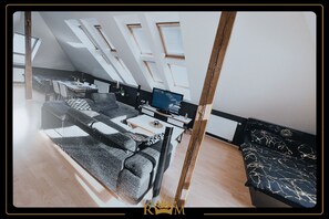 Et moderne loftværelse med ovenlys, sofa, fjernsyn og spiseplads.
