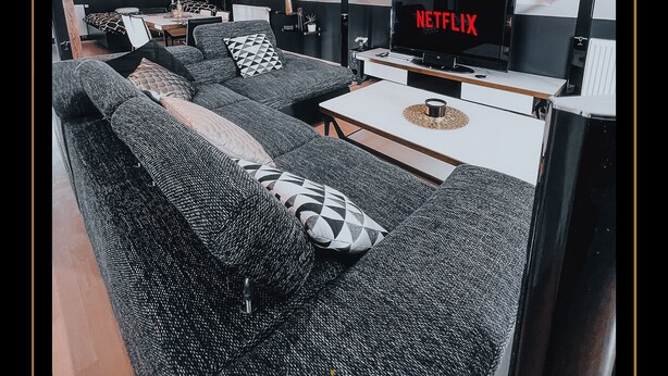 Een moderne woonkamer met een hoekbank, een salontafel en een televisie waarop het Netflix-logo staat.