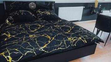 Une chambre à coucher moderne avec une couvre-lit noire ornée de motifs dorés, un radiateur blanc et un bureau avec une chaise.