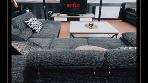 Een moderne woonkamer met een grote flatscreen-tv, gestreeptgrijze banken, een salontafel en dakramen.