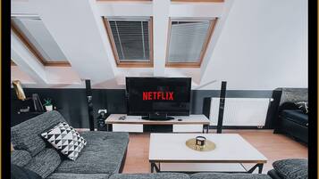 Una sala de estar moderna con un televisor de pantalla plana grande, sofás grises con estampado, una mesa de centro y tragaluces.