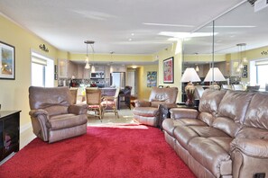 A living room with leather sofas, a red carpet, and a kitchen in the background. - XPLORIE ACTIVITIES & LINENS INCLUDED*! Direct Oceanfront 3BR/2BA condo in The Plaza. Indoor and Outdoor Pools and Tiki Bar. (Ocean City)
