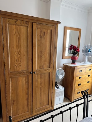 A wooden wardrobe with two doors, a dresser with drawers, a mirror, and a fan.