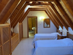 A bedroom with two beds, wooden furniture, and a sloped ceiling.