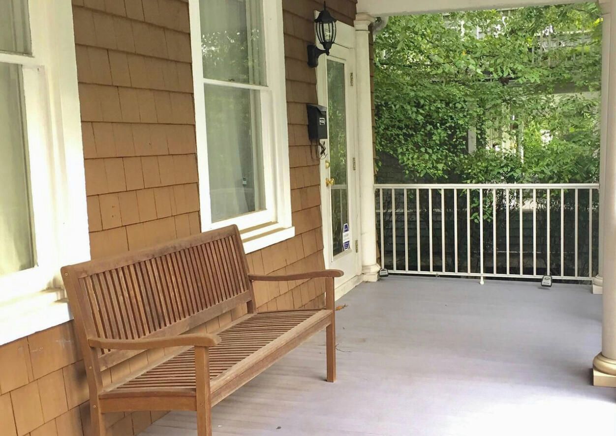 A wooden bench on a porch with a white railing and a view of trees.