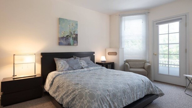 Une chambre à coucher avec un lit, des lampes de chevet, une chaise, une porte et une fenêtre.