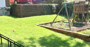 Un patio trasero con un columpio, un muro de ladrillo y un seto.