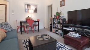 Un salon comprenant un canapé, une table basse, un téléviseur, une bibliothèque et un coin repas avec des chaises et une table.