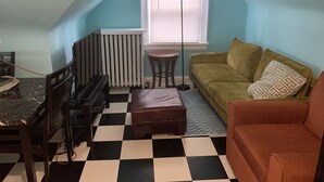 Ein gemütliches Dachzimmer mit kariertem Boden, einem grünen Sofa, einem braunen Sessel, einem kleinen Tisch und einem Heizkörper.