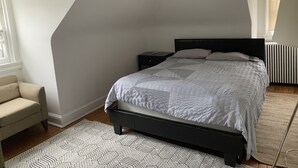 Ein Schlafzimmer mit Bett, Nachttisch, Sessel und Heizkörper.