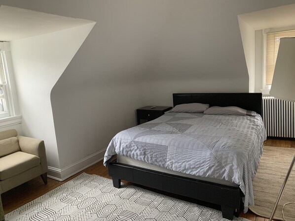 A bedroom with a bed, nightstand, chair, and radiator.