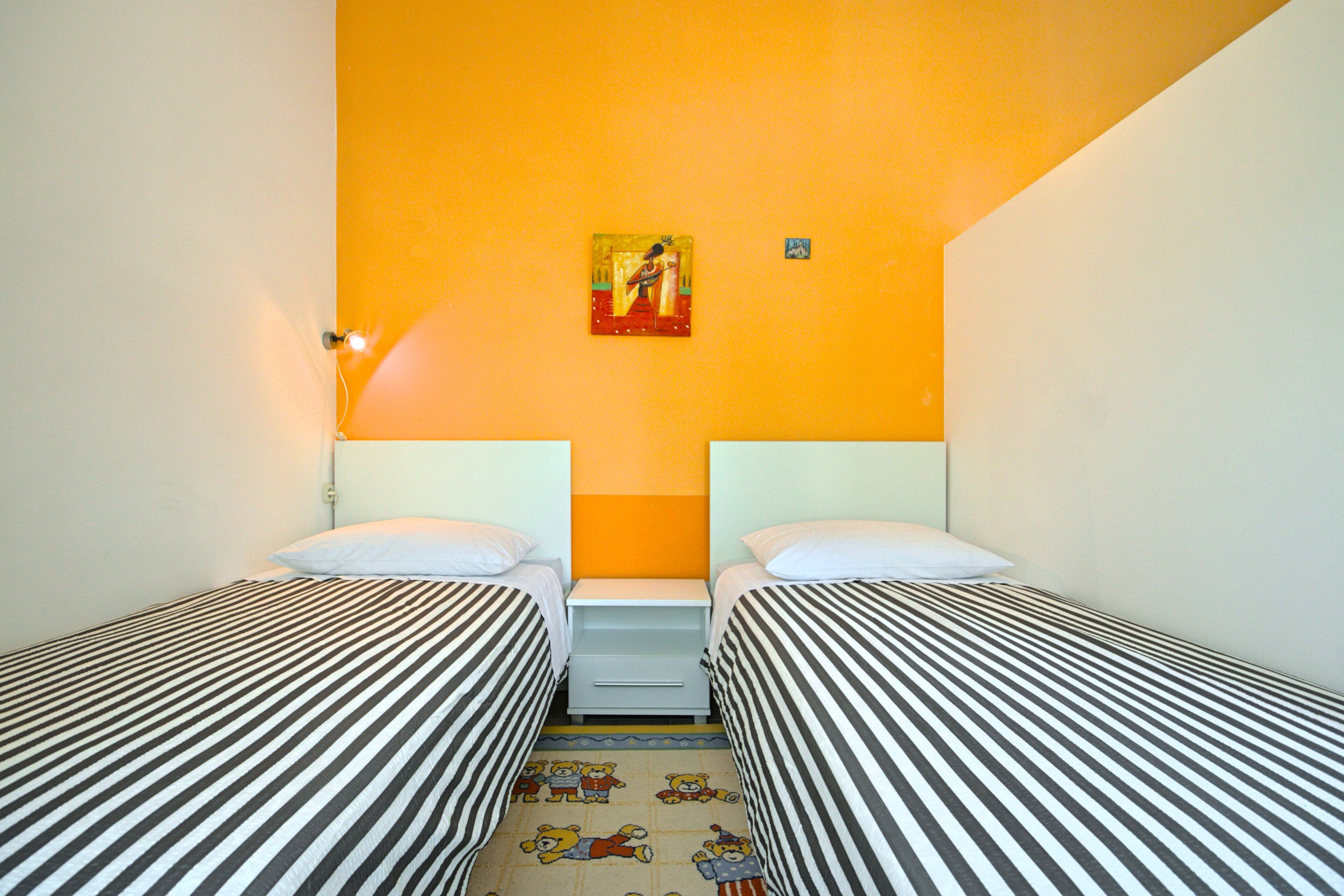 A room with two single beds, a nightstand, a small table, and a wall-mounted painting.