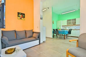 Una sala de estar con sofá, una mesa de comedor con sillas y una cocina con armarios y encimera.