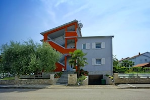 Un edificio de dos pisos con una escalera, un balcón y un pequeño jardín.