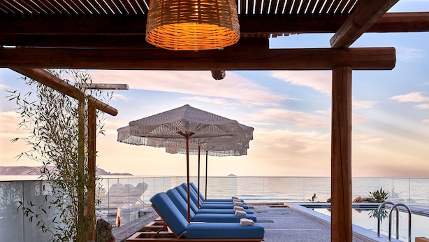 Zona de piscina en la azotea con sillas de descanso y un gran parasol, con vistas a una masa de agua.