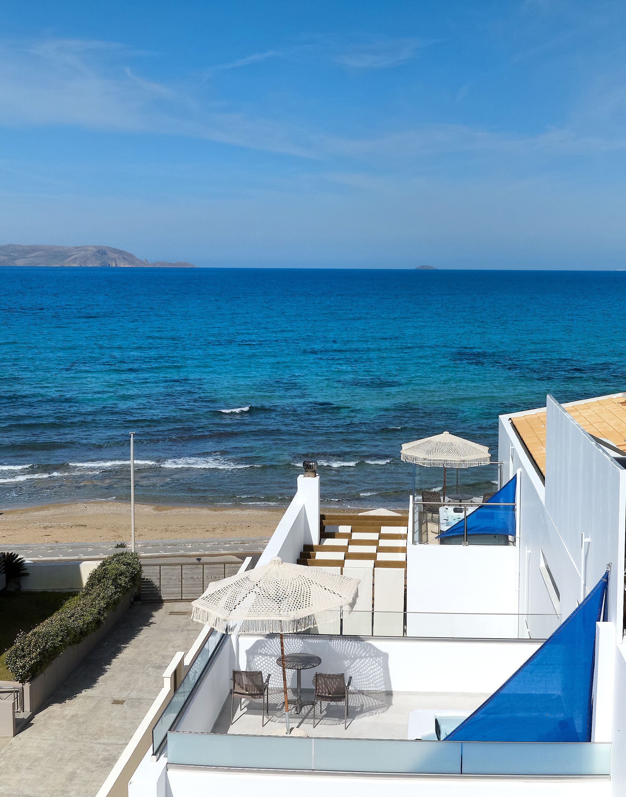 A rooftop terrace with a view of the sea, outdoor seating, and a white building.