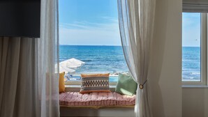 Una habitación con ventana que da al mar, con cama, almohadas y televisión en la pared.