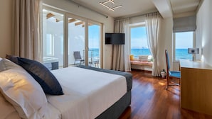 Habitación de hotel con una cama grande, un escritorio, un televisor y un balcón con vista al mar.