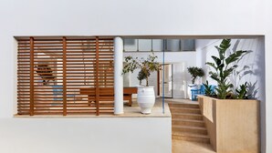 Un interior moderno con un separador de listones de madera, un jarro blanco, una escalera y una jardinera con plantas de hojas grandes.