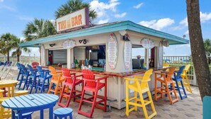 Eine Tiki-Bar mit bunten Stühlen und Tischen, einer Speisekarte und blauem Himmel.