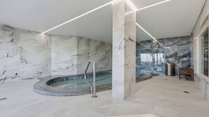 Ein moderner Wellnessbereich mit Whirlpool, Marmorwänden und einer Holzbank.