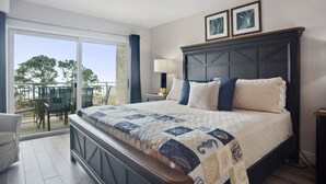 A bedroom with a large bed, a nightstand, a lamp, and a view of the outdoors.