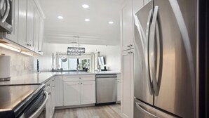 A modern kitchen with stainless steel appliances, white cabinetry, and a wooden floor.