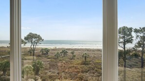 A beach view from a window with a clear sky, sandy beach, and sparse vegetation.