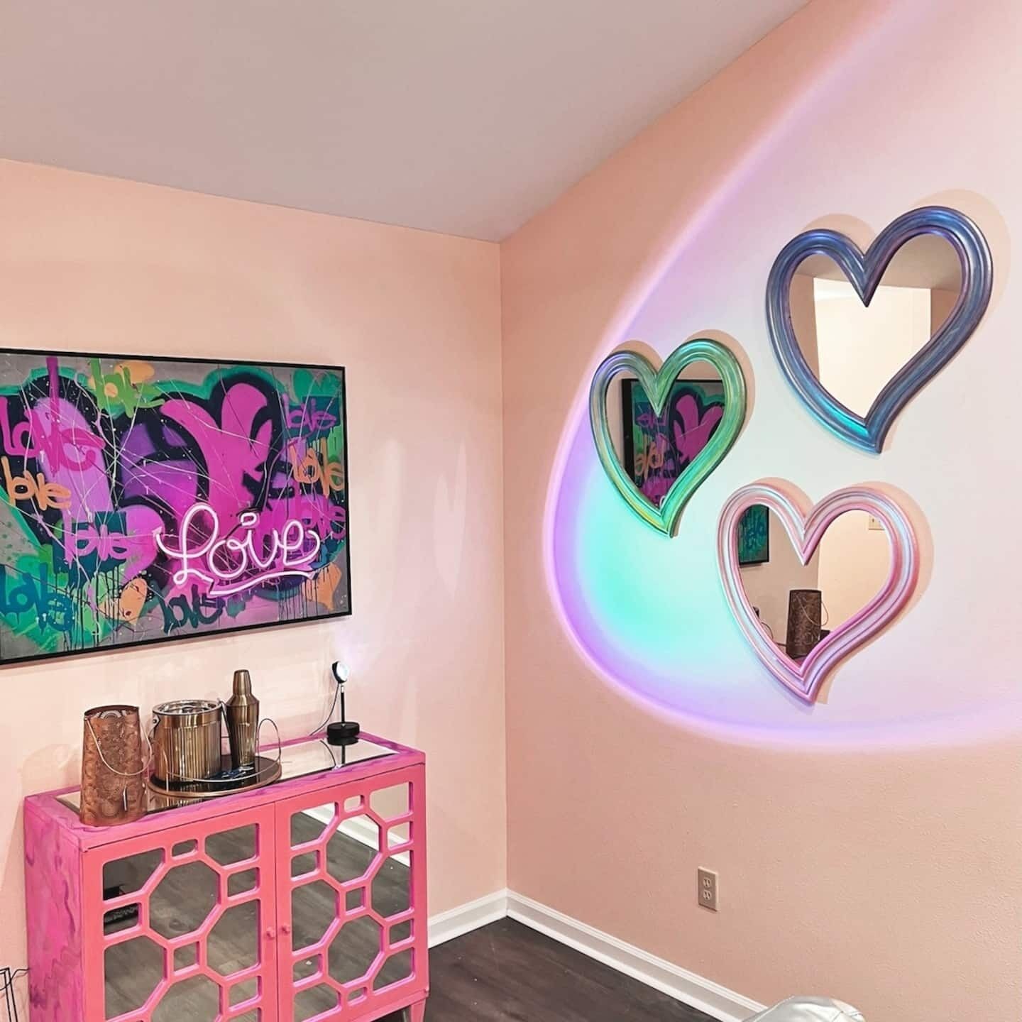 Een kamer met een roze muur, een graffiti kunstwerk en drie spiegelhartjes.