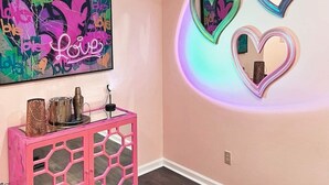 Ein Zimmer mit einer rosafarbenen Wand, einem Graffiti-Kunstwerk und drei herzförmigen Spiegeln.