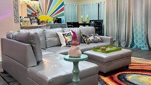 Ein modernes Wohnzimmer mit einem grauen Ecksofa, einem kleinen runden Tisch und einem farbenfrohen Teppich.